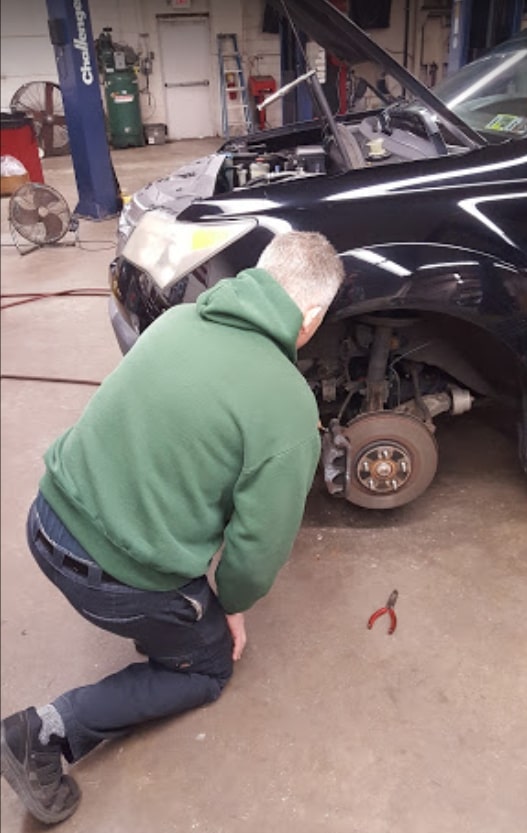 A man is repairing a car in the garage, working on maintenance or repairs